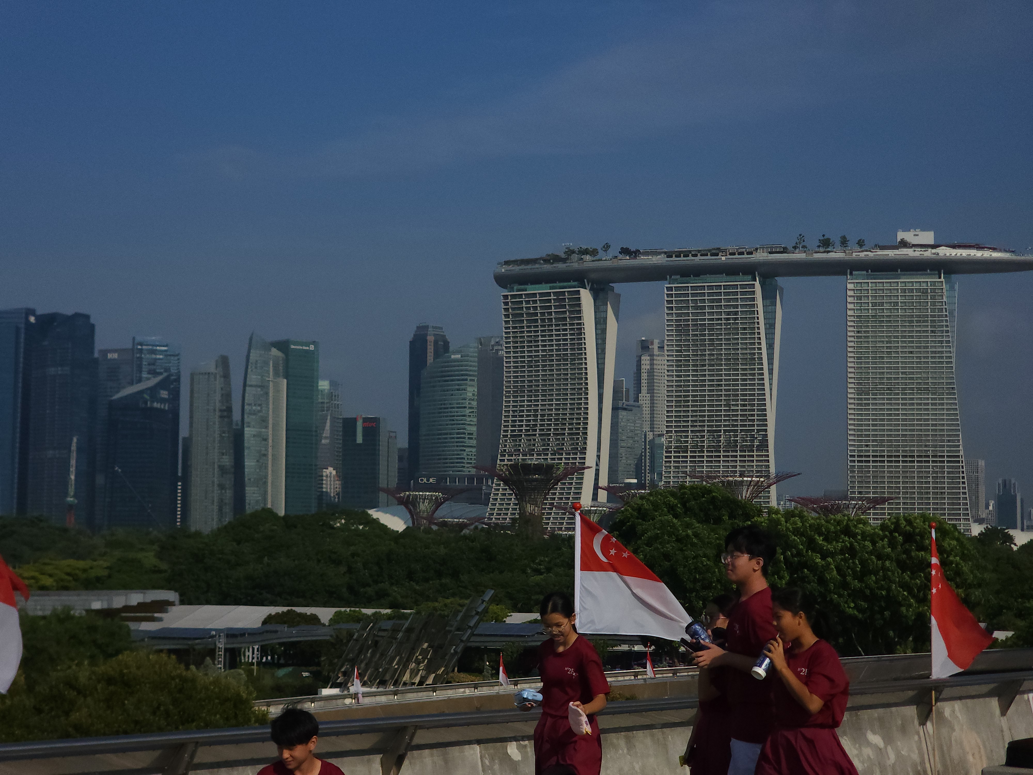 Marina Bay Sands beneath a dark stormy sky, with Singapore flags in the foreground