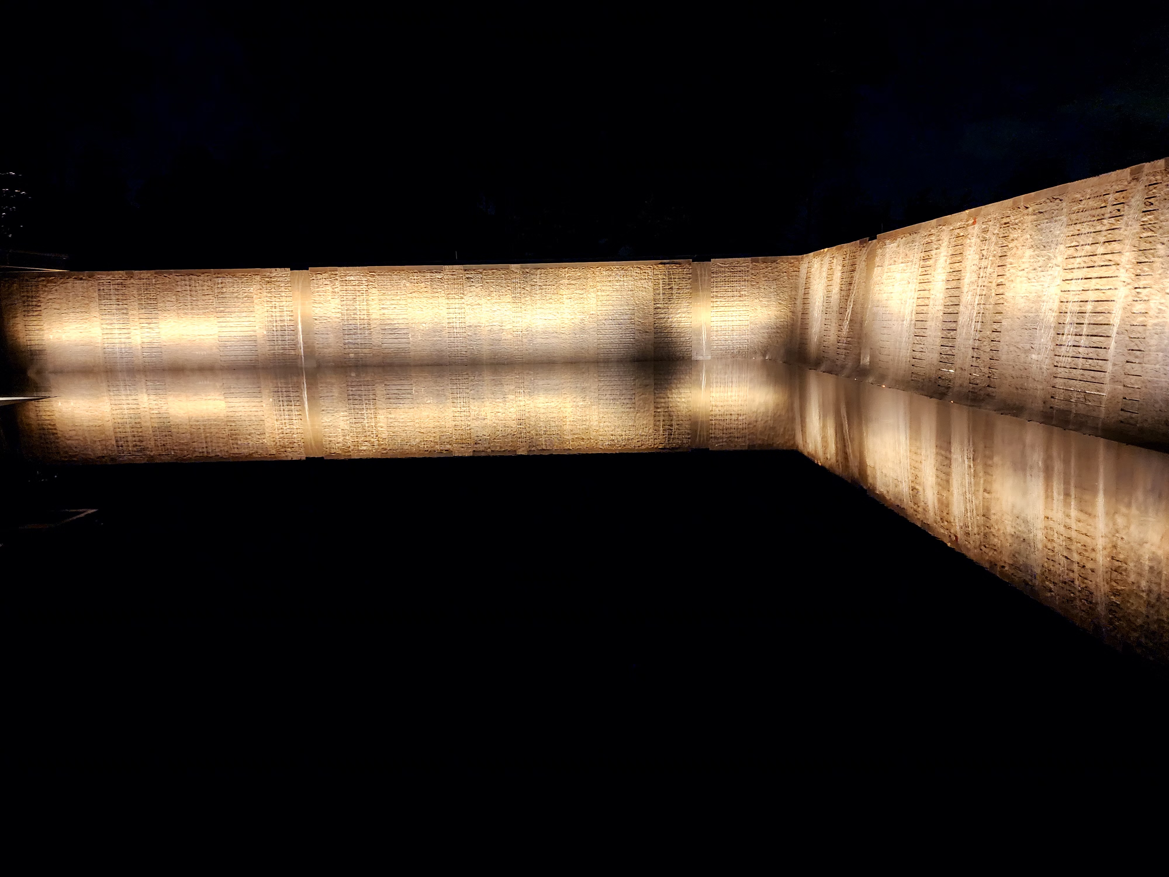A lit stone wall reflected in still water at night