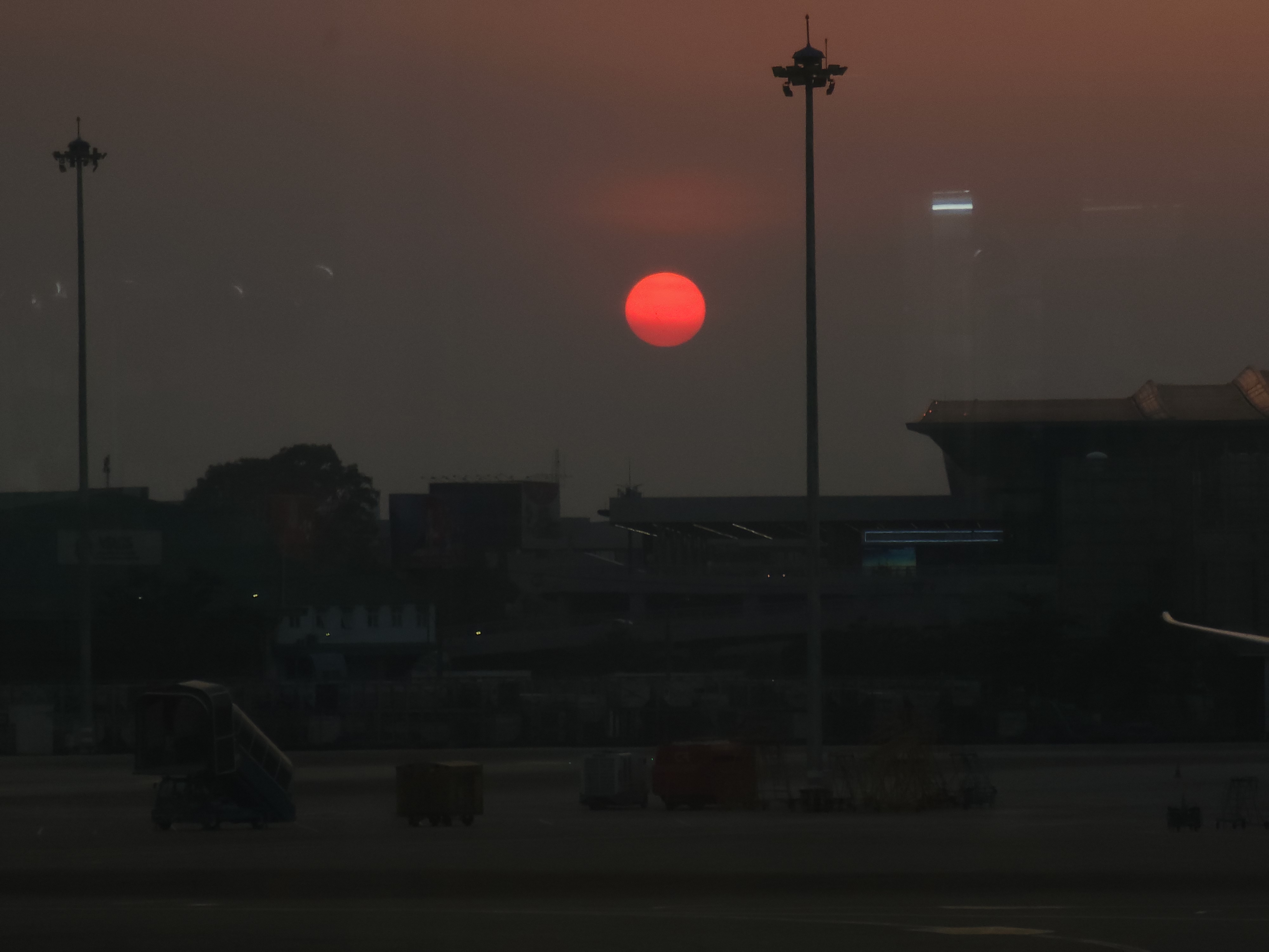 A red sun suspended in haze between two streetlights